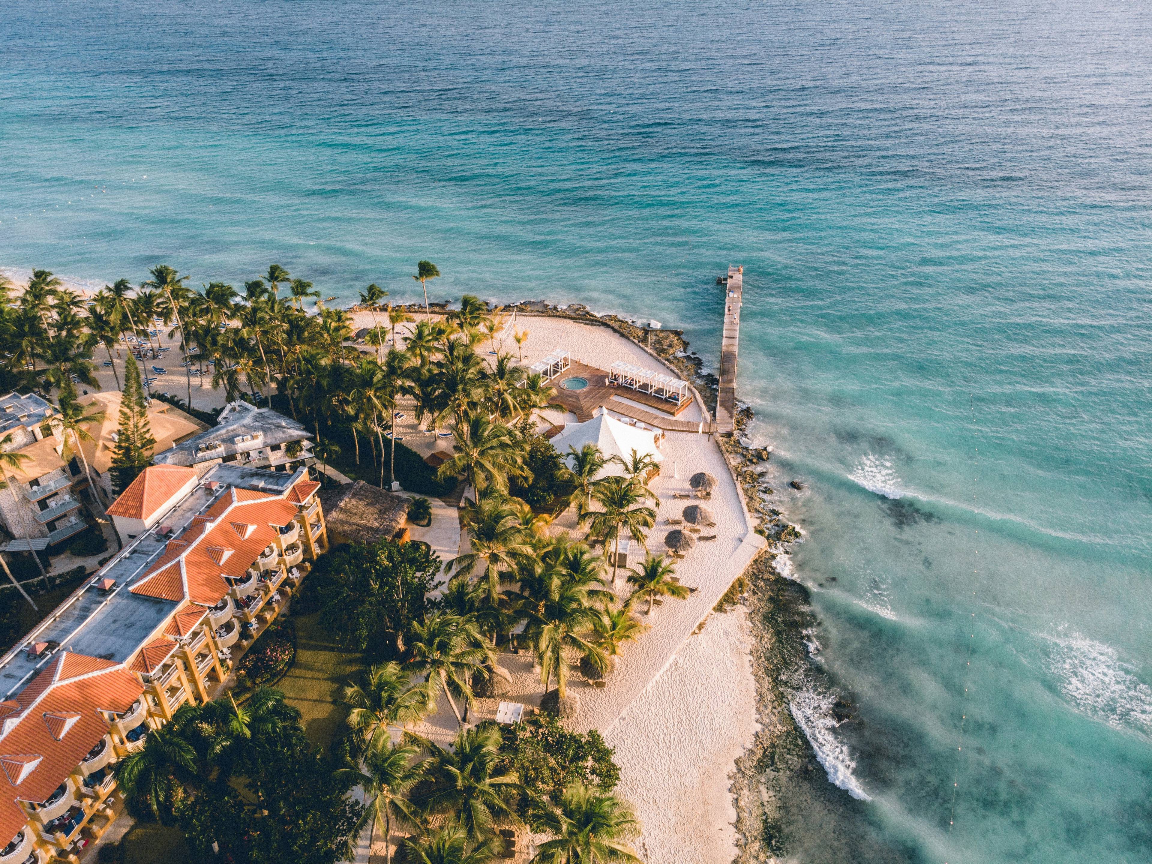 Vista aérea de una hermosa playa con palmeras y un hotel cercano.