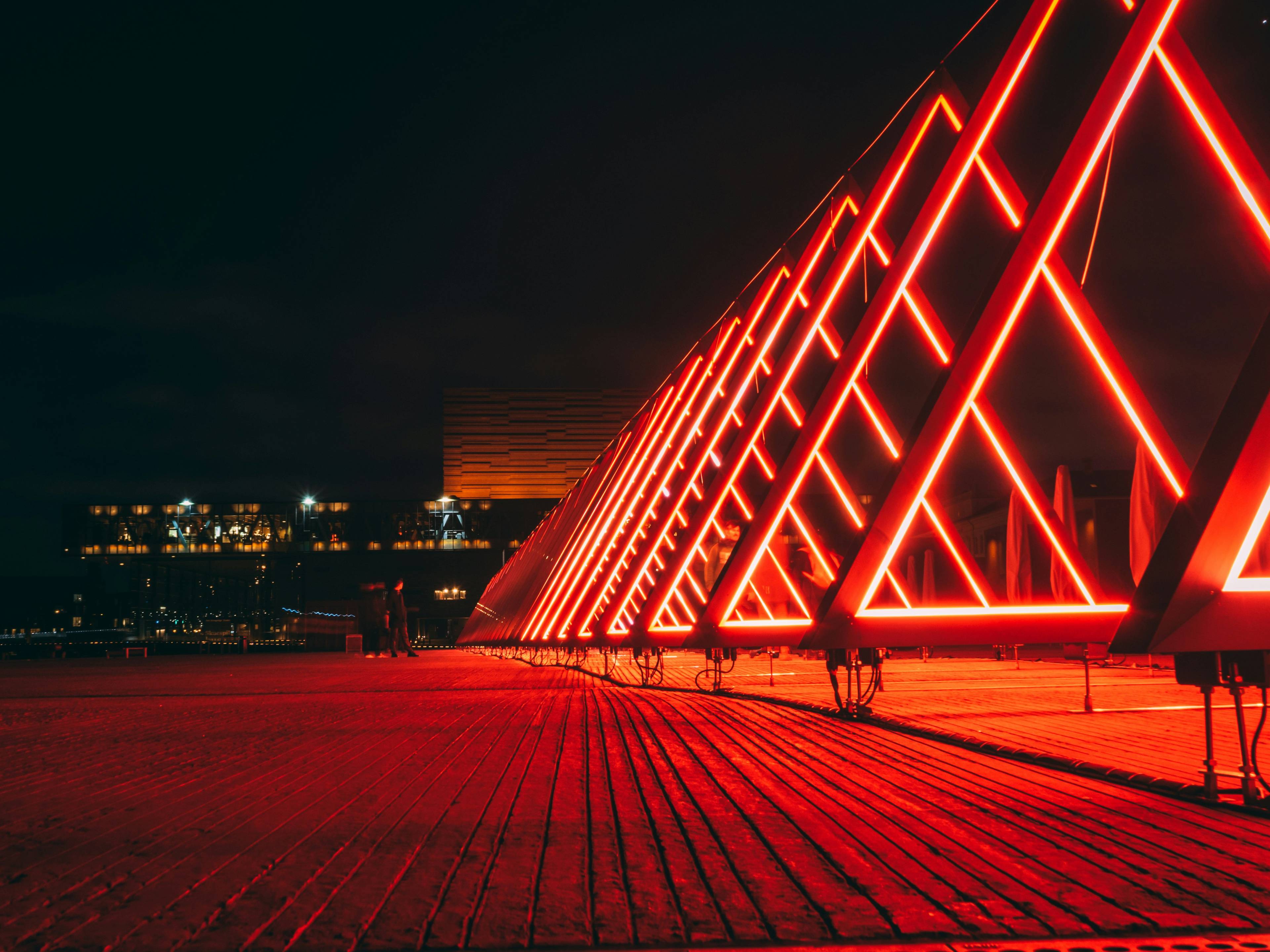 toms-uluks-hadioqbon7w-unsplash-a984629f-3e11-454e-8039-7be62a379d26 Una serie de estructuras en forma de triángulo iluminadas con luces rojas en un entorno nocturno.