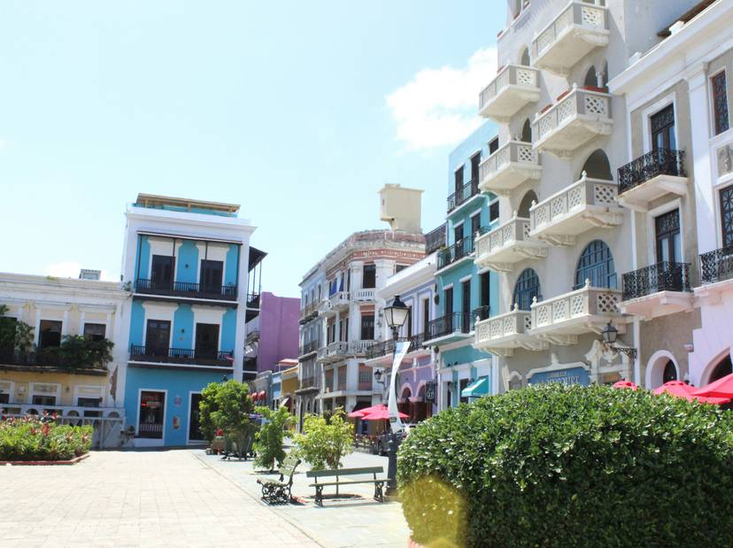 Una calle colorida con edificios de arquitectura colonial y terrazas de restaurantes bajo sombrillas rojas.