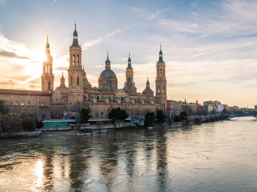 pedro-sanz-dvgai6nx83s-unsplash Vista de la Basílica del Pilar en Zaragoza al atardecer, reflejada sobre las aguas del río Ebro.