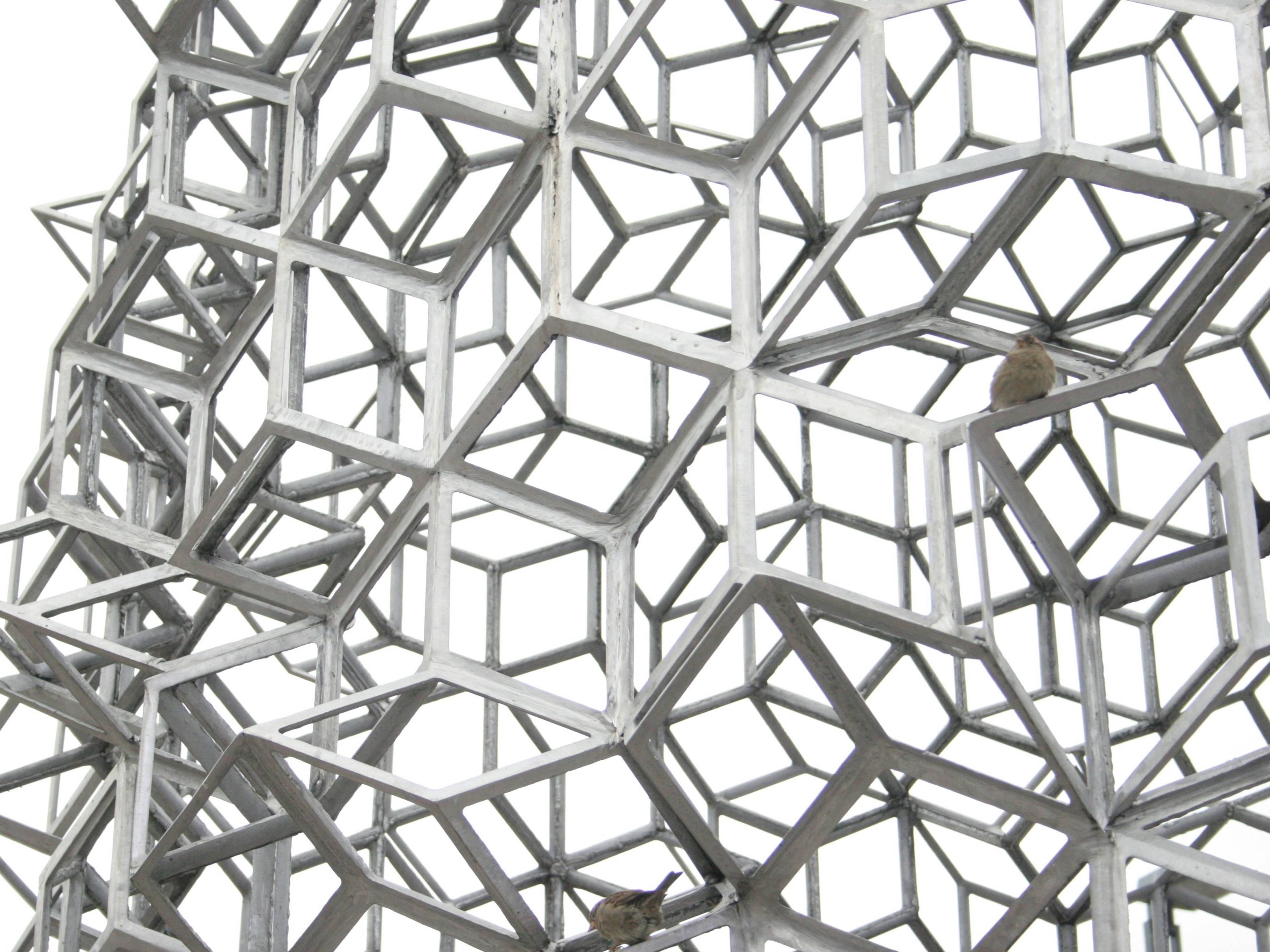 tasha-kostyuk-pmq89avufq-unsplash-42ce42fd-3380-4533-8e9e-53931f499b9f Estructura geométrica hecha de cubos interconectados en color metálico.
