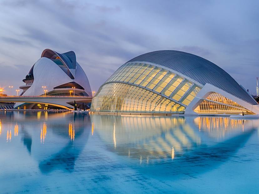 valencia-1049389-1280 Vista del complejo arquitectónico moderno con estructuras futuristas reflejadas sobre un cuerpo de agua al atardecer.