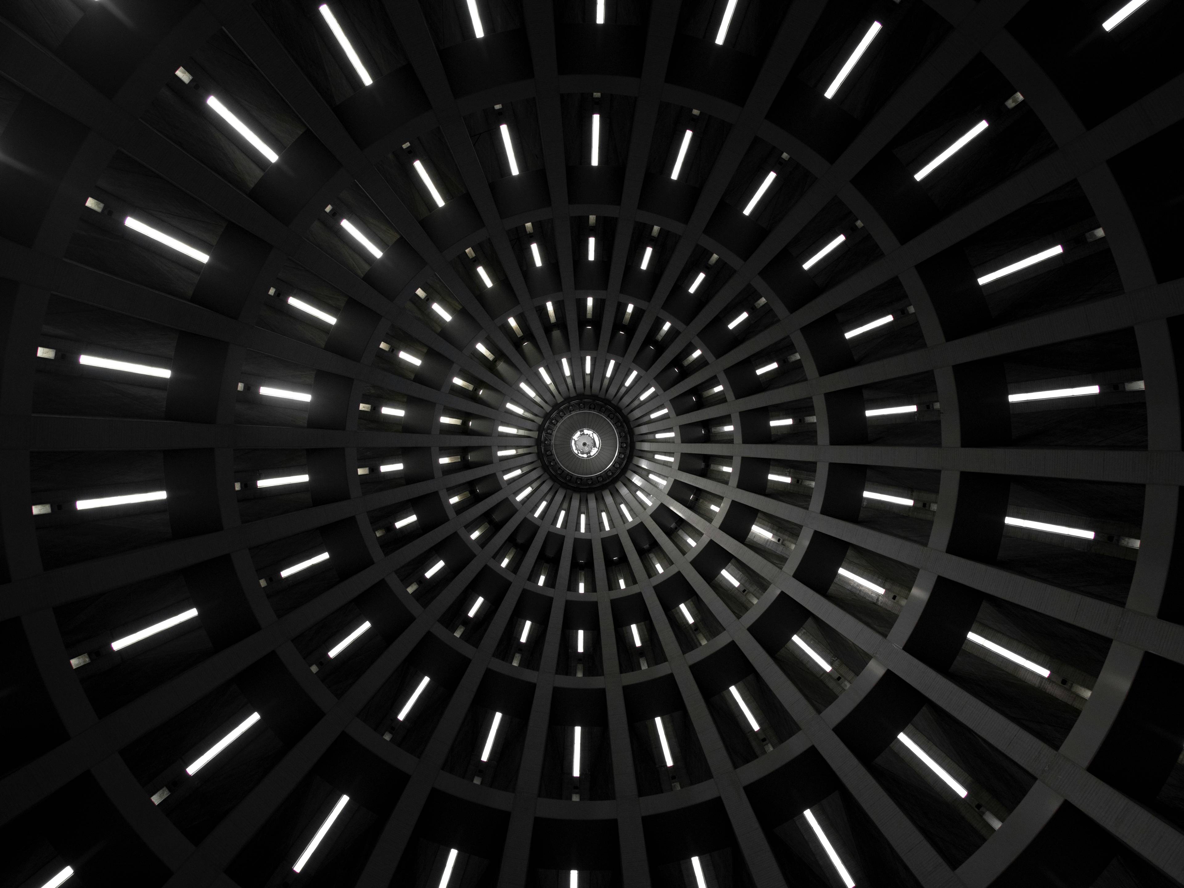 Una vista desde abajo de una estructura circular con luces que emanan de las paredes en un patrón radial.