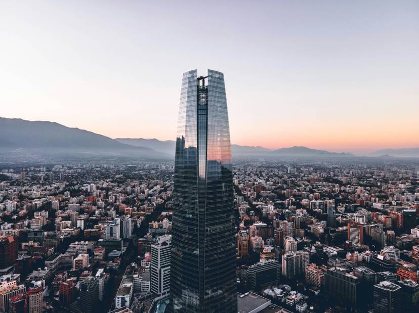 Vista aérea de una ciudad moderna al atardecer, destacando un rascacielos de vidrio en primer plano.