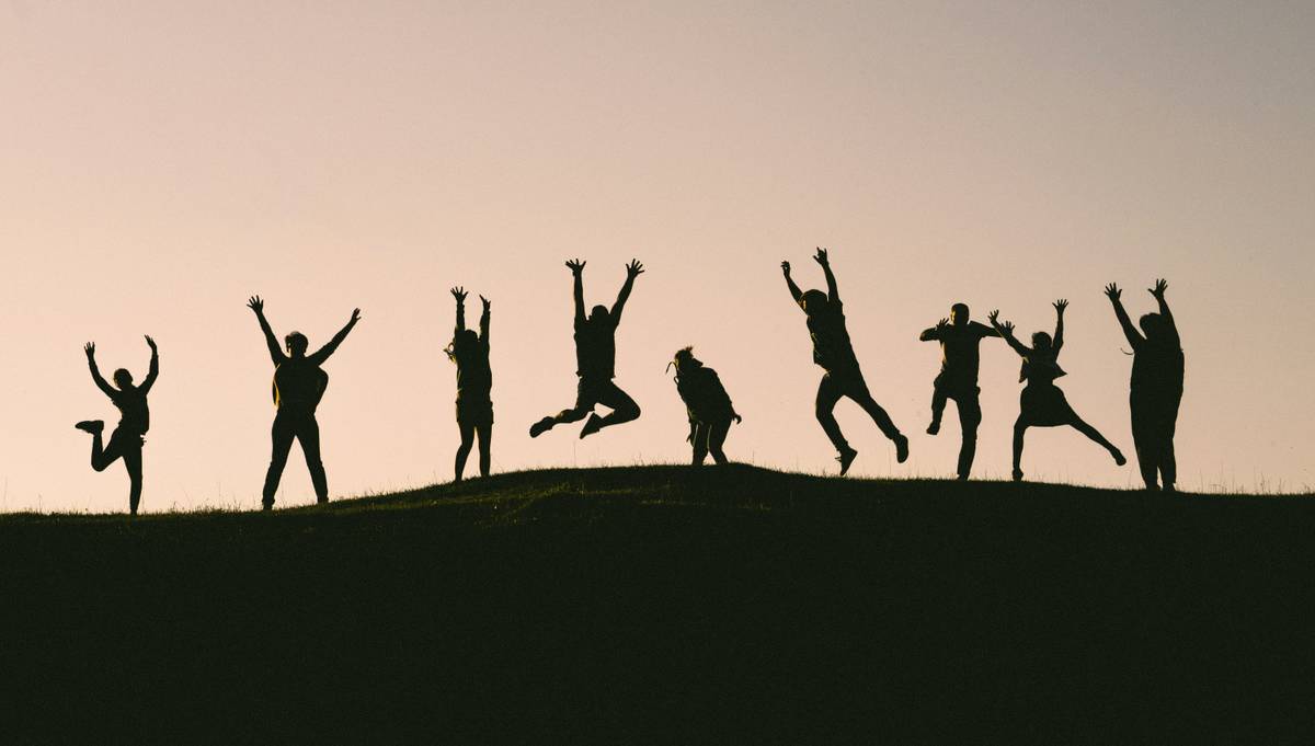 Un grupo de personas en silueta saltando y levantando las manos al aire en un atardecer.