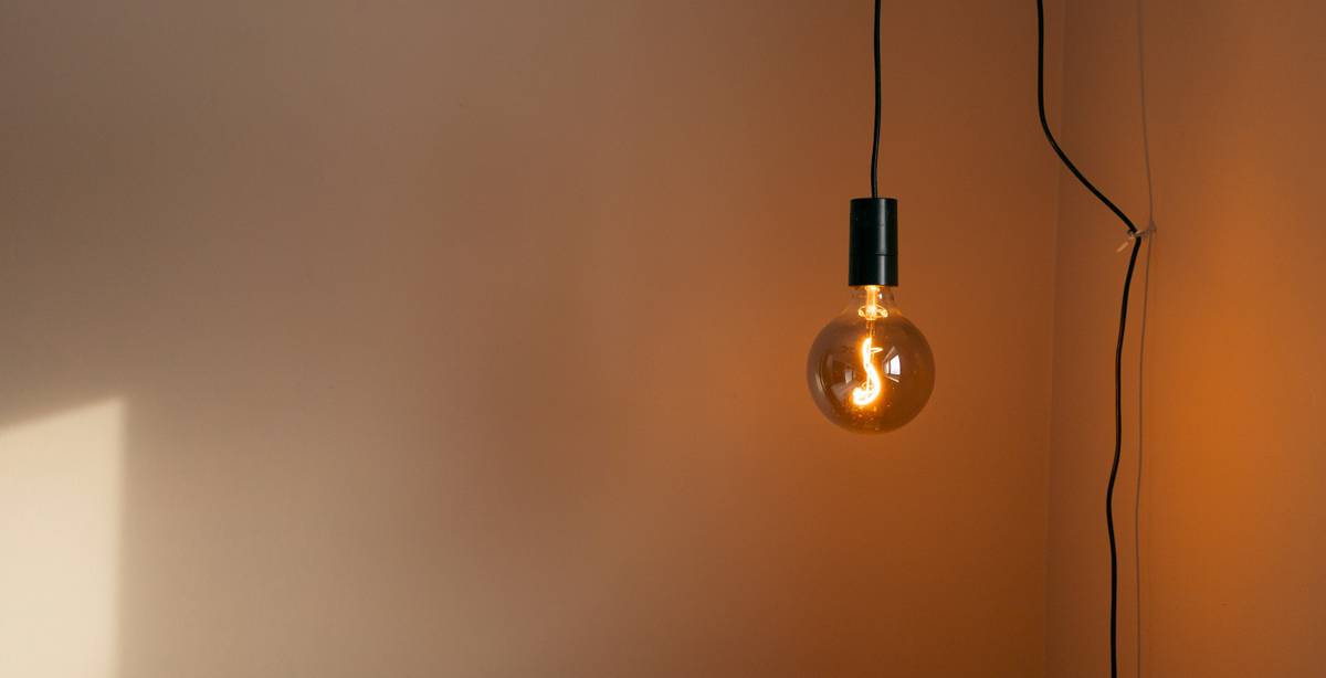 Una bombilla colgante emite luz suave en una pared clara.