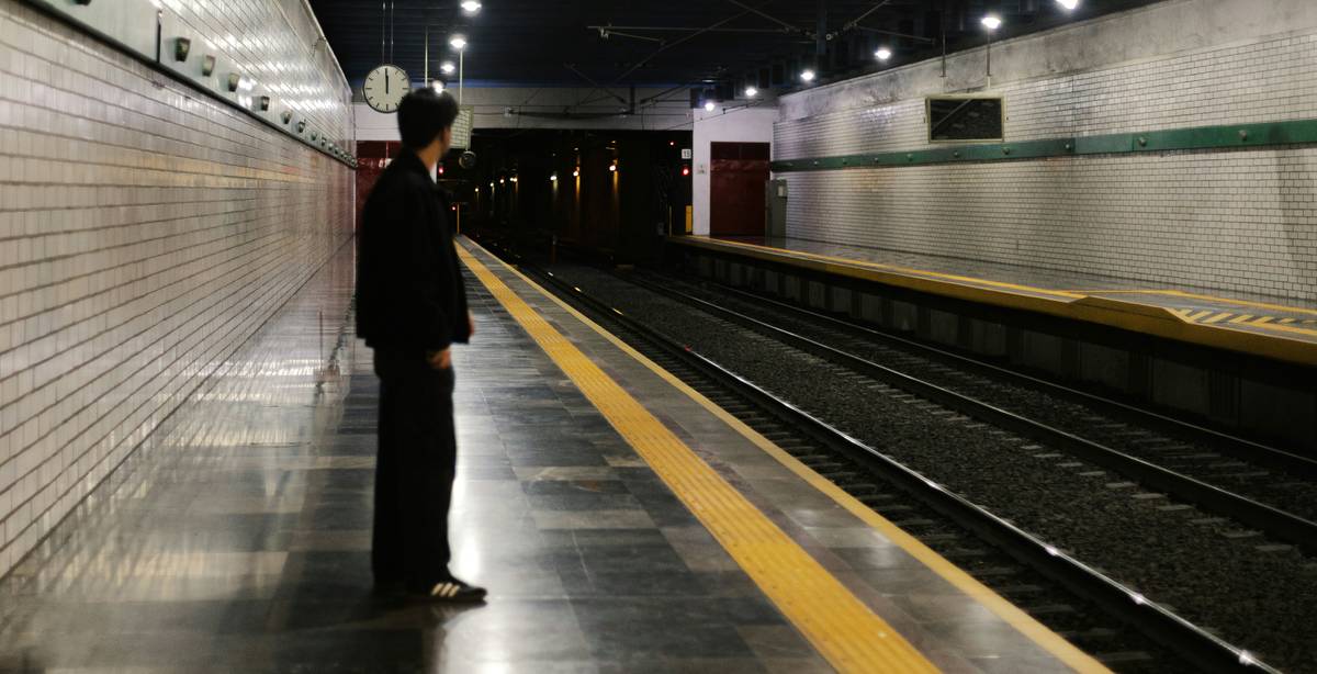 Un hombre espera en una estación de tren vacía y oscura.
