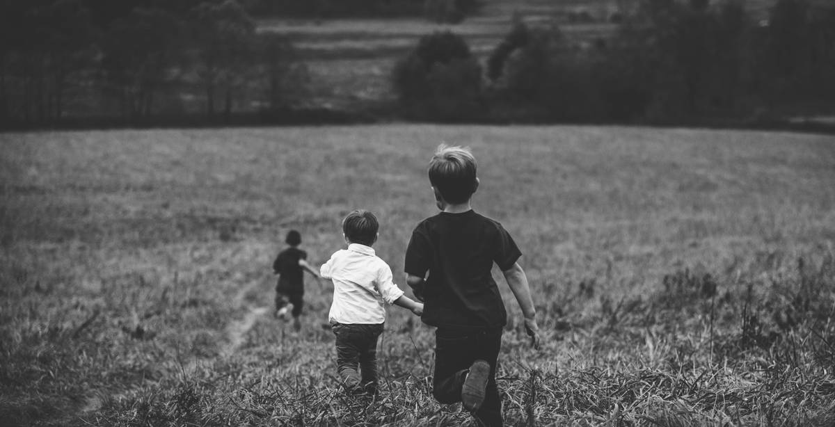 Un grupo de niños corre por un campo verde hacia un paisaje natural.