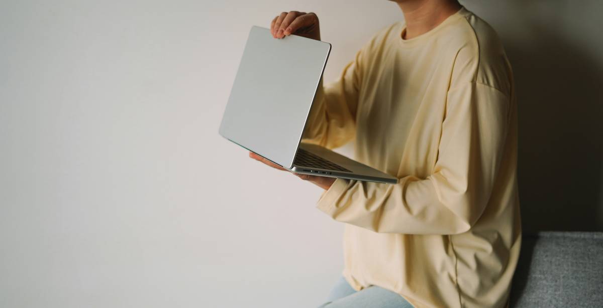 Una persona sostiene una computadora portátil mientras se sienta en un sofá.