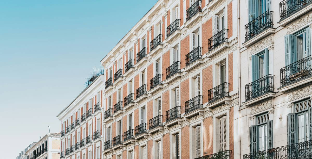 Una imagen de edificios en una calle de la ciudad con balcones y un cielo despejado.