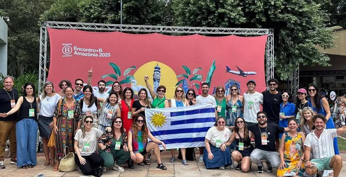 Un grupo de personas sonrientes posando frente a un telón decorativo con símbolos de Uruguay y el logotipo de un evento.