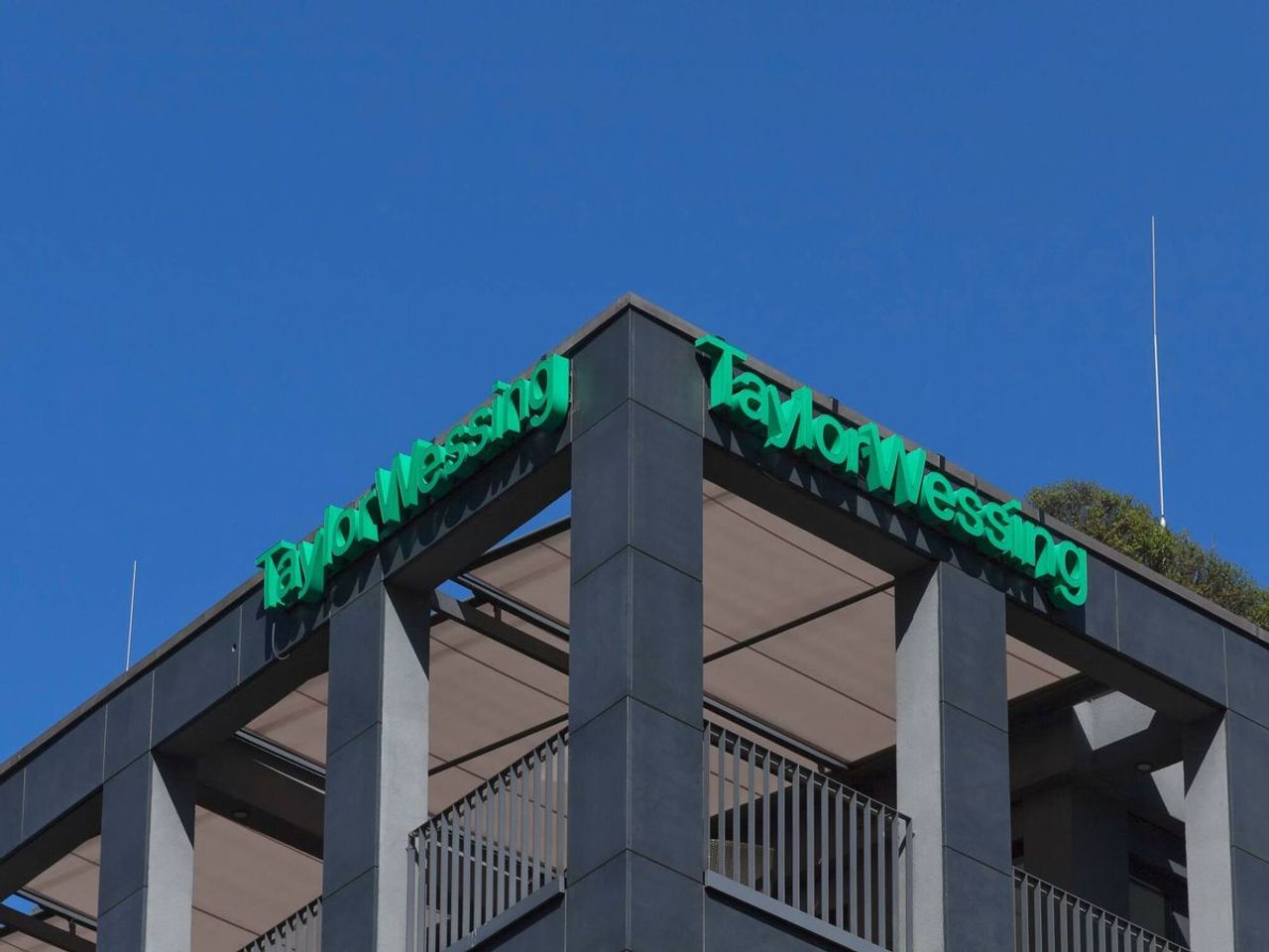 Una esquina de un edificio moderno con el letrero de 'Taylor Wessing' en color verde.