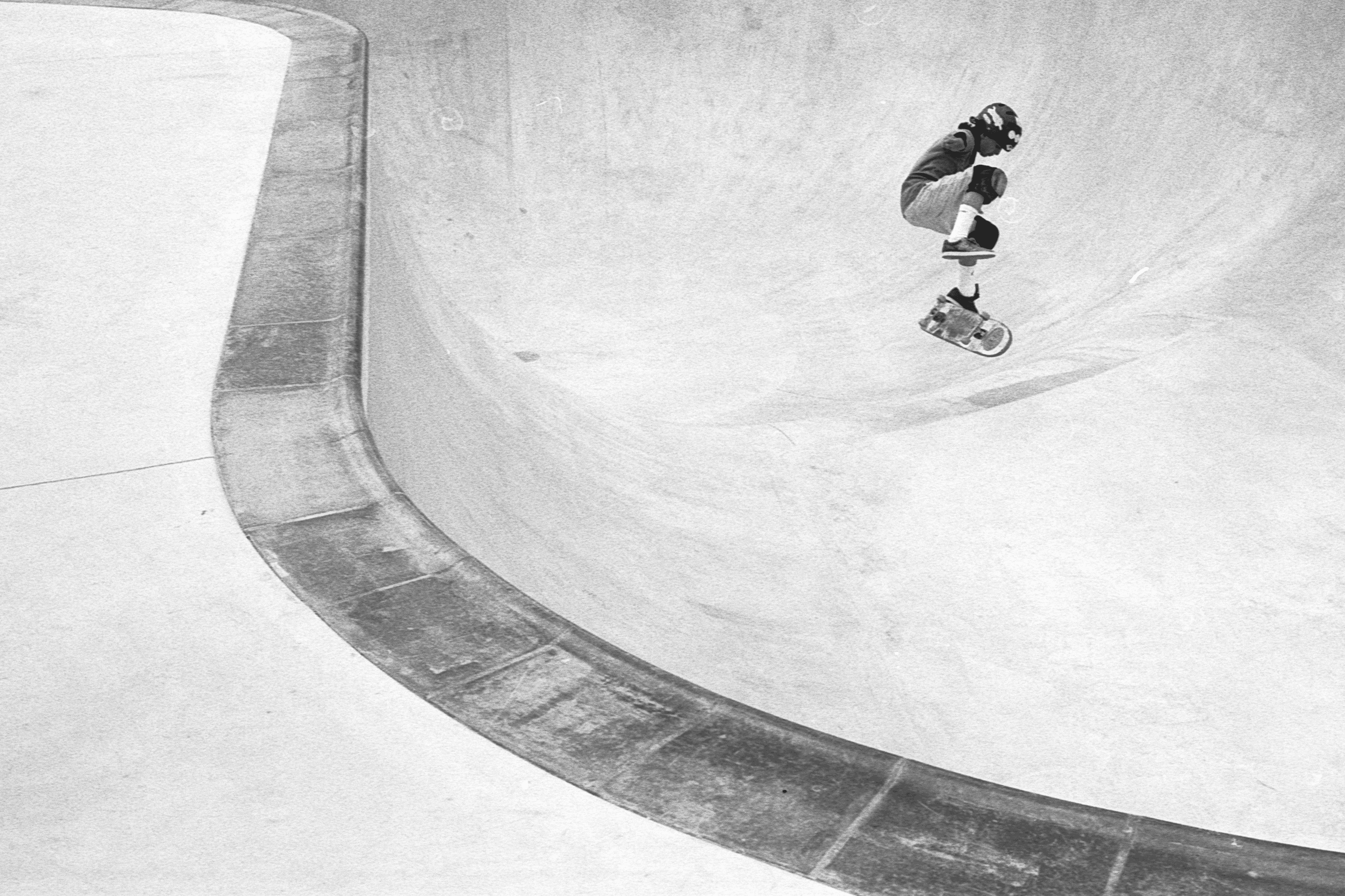 Un skater realiza un truco en un bowl de patinaje en una imagen en blanco y negro.